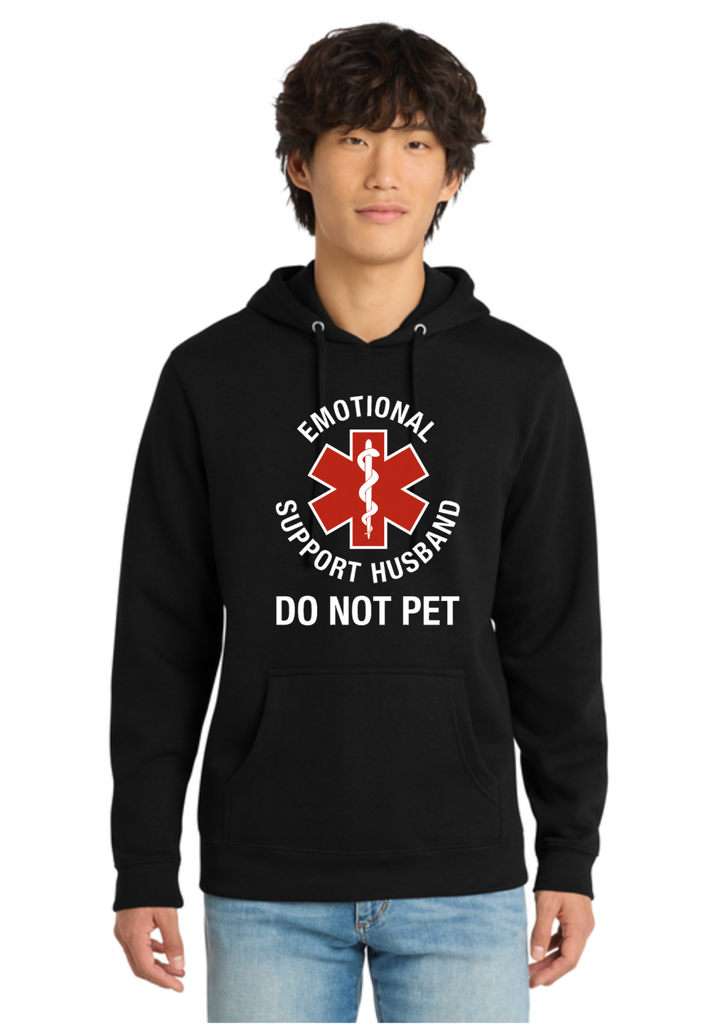 A man wearing a black pullover hoodie with a red and white graphic that reads 'EMOTIONAL SUPPORT HUSBAND DO NOT PET' on the front, paired with light blue jeans, against a plain white background.