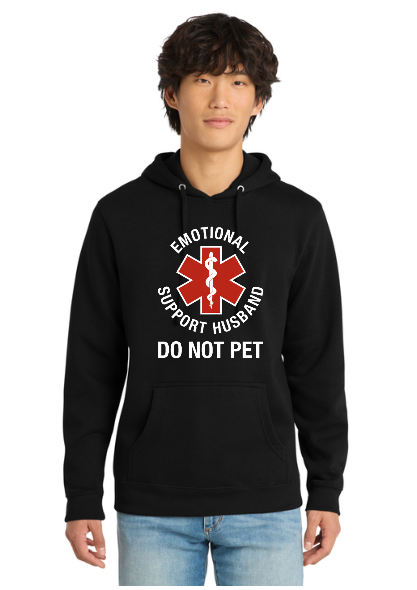 A man wearing a black pullover hoodie with a red and white graphic that reads 'EMOTIONAL SUPPORT HUSBAND DO NOT PET' on the front, paired with light blue jeans, against a plain white background.