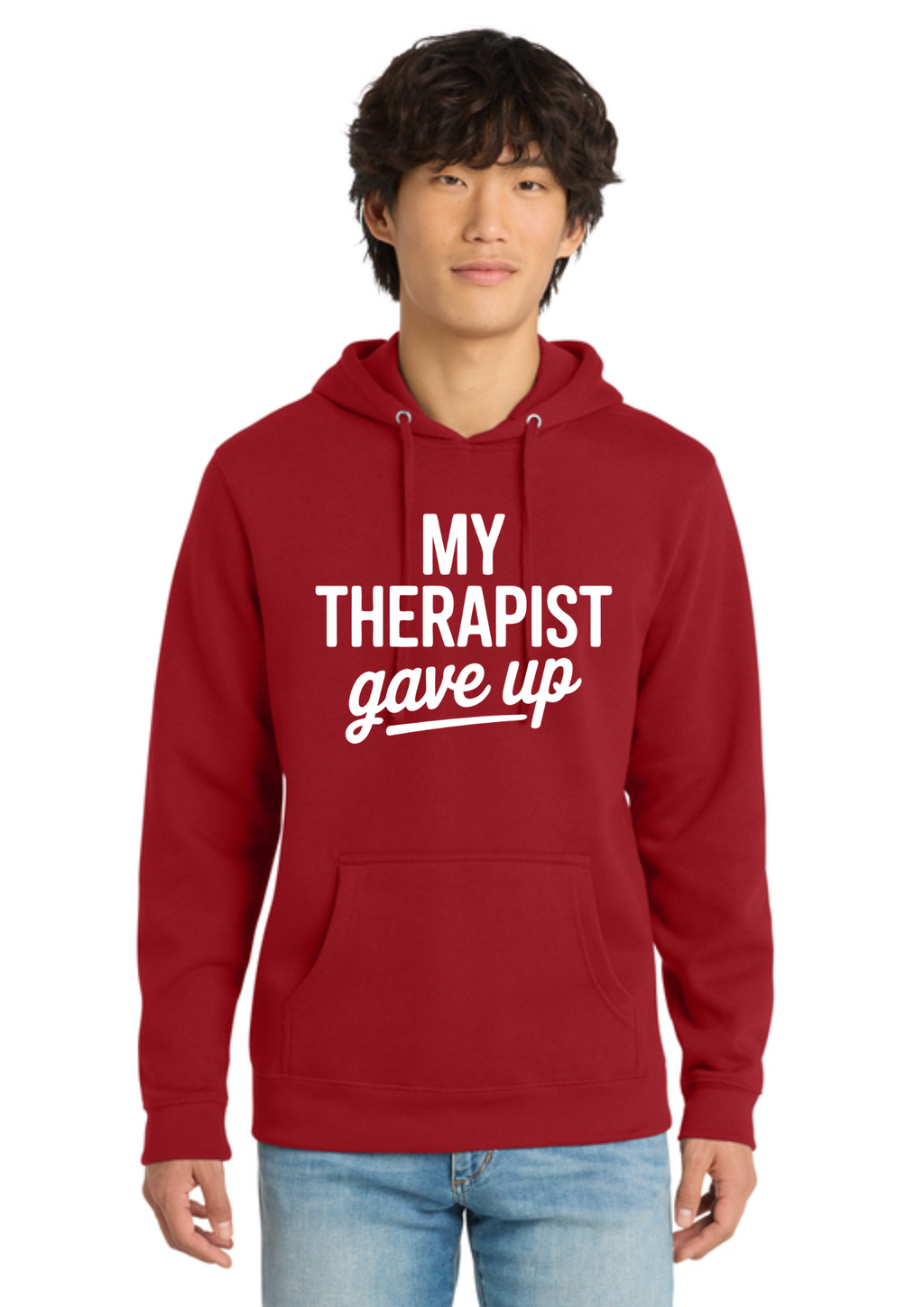A man wearing a red pullover hoodie with the white printed text 'MY THERAPIST gave up' on the chest, paired with light blue jeans, against a plain white background.