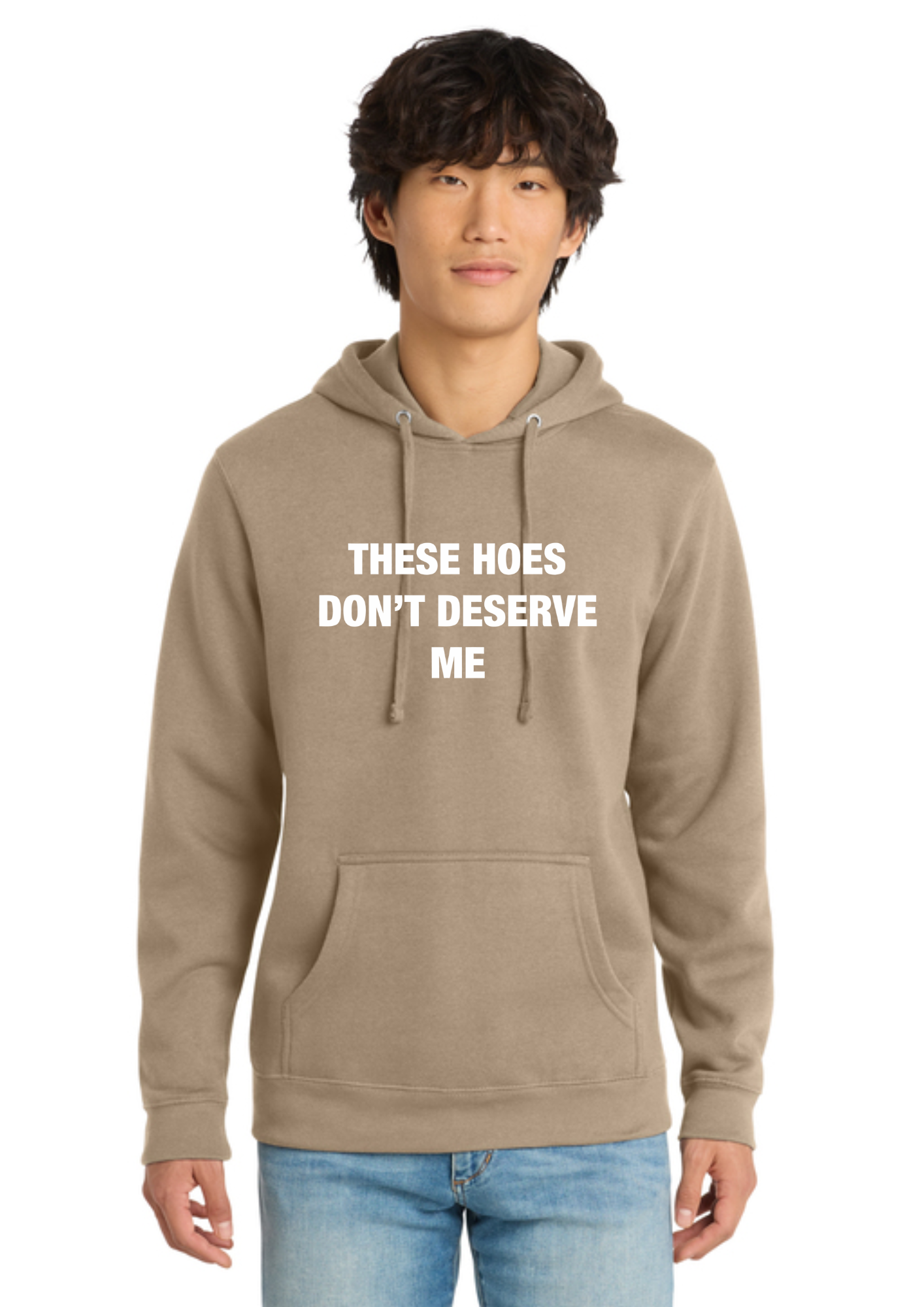 A man wearing an olive green pullover hoodie with the text 'THESE HOES DON'T DESERVE ME' printed in white on the chest, paired with blue jeans, against a plain white background.