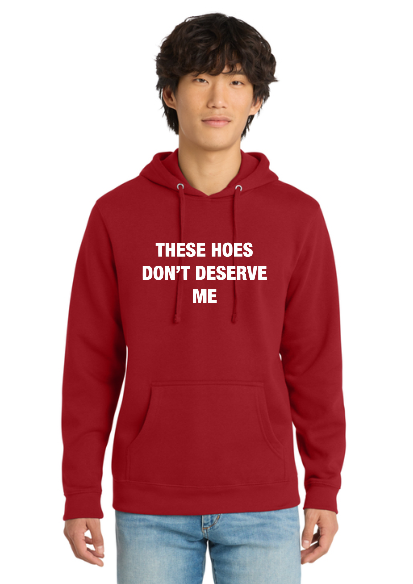 A man wearing a red pullover hoodie with the text 'THESE HOES DON'T DESERVE ME' printed in white capital letters on the chest, paired with blue jeans, against a plain white background.