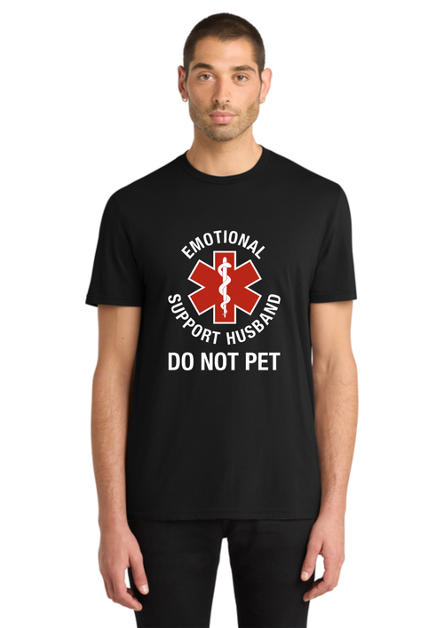 A man wearing a black short-sleeve t-shirt with a graphic print that reads 'EMOTIONAL SUPPORT HUSBAND DO NOT PET' around a red and white star-of-life style medical symbol, shown against a plain white background.