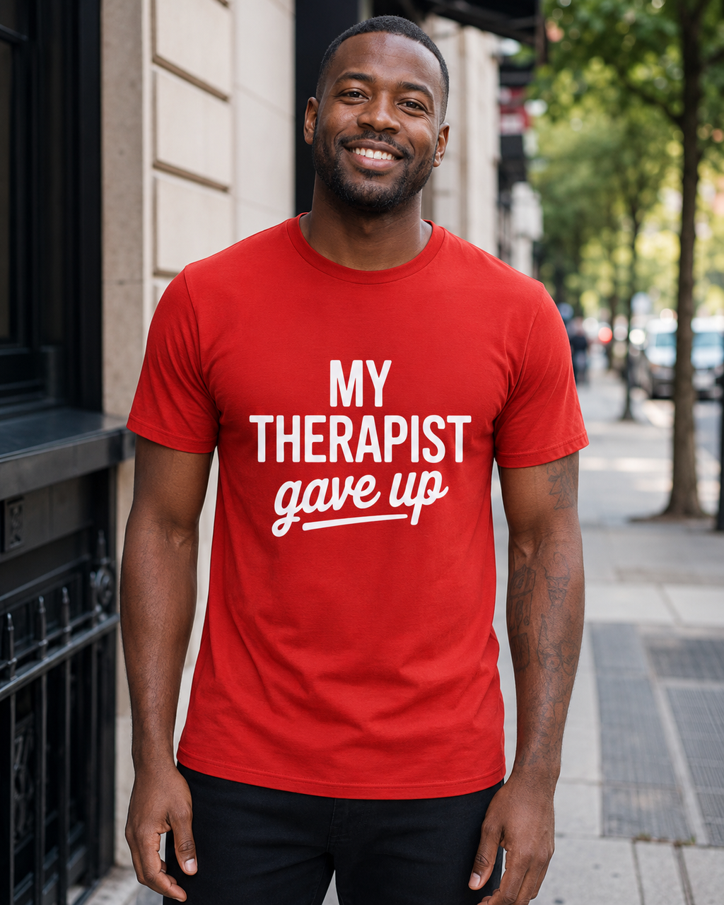 A man wearing a bright red crewneck t-shirt with the white printed text 'MY THERAPIST gave up' stands on a city sidewalk.