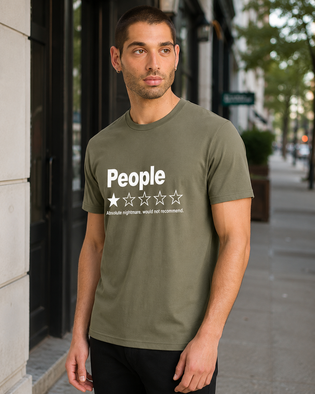 A man wearing an olive green t-shirt with a white graphic that reads 'People' and a one-star rating, standing on a city sidewalk.
