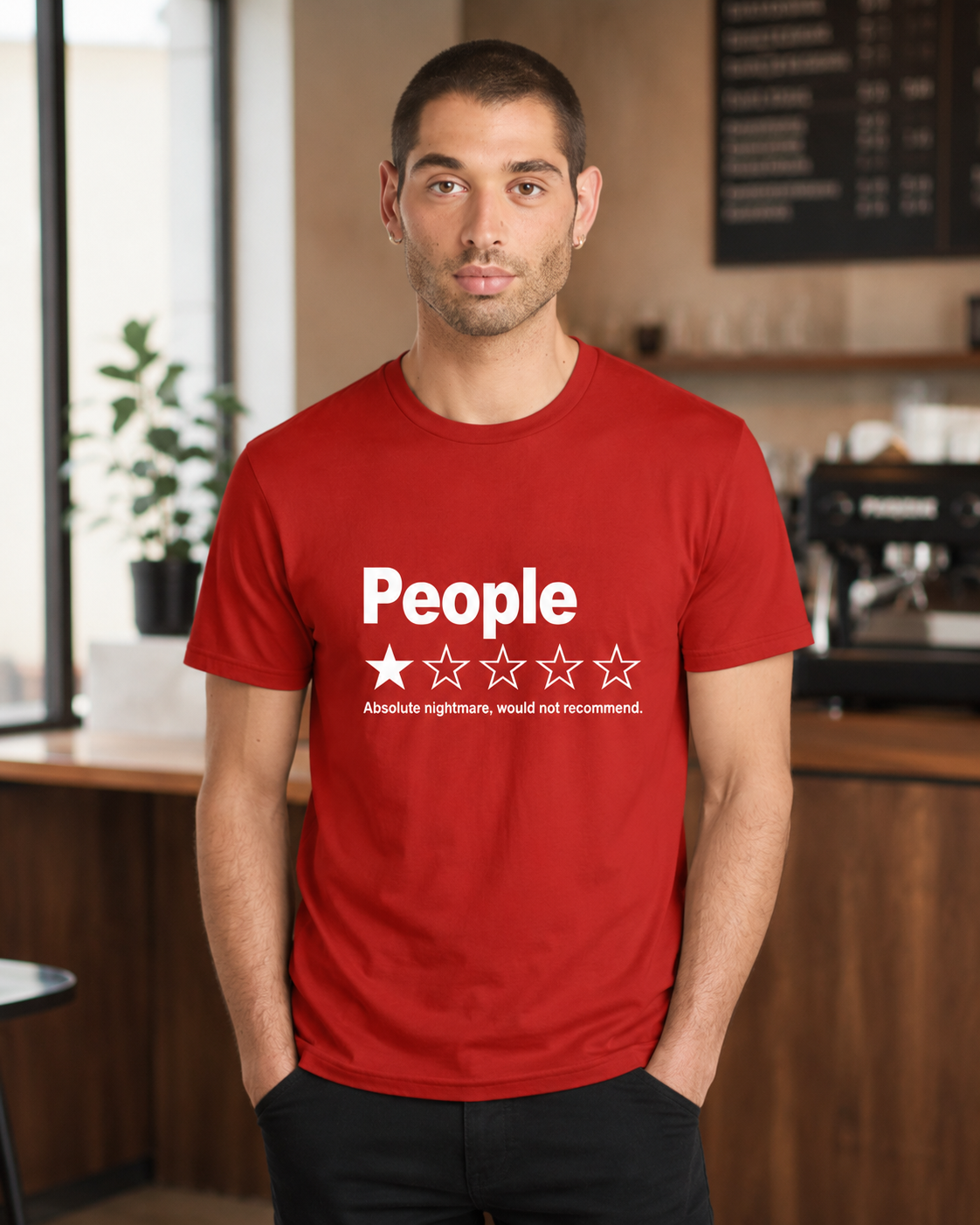 A man wearing a red crewneck t-shirt with a white graphic that reads 'People' and a one-star review design, standing in a cafe environment.