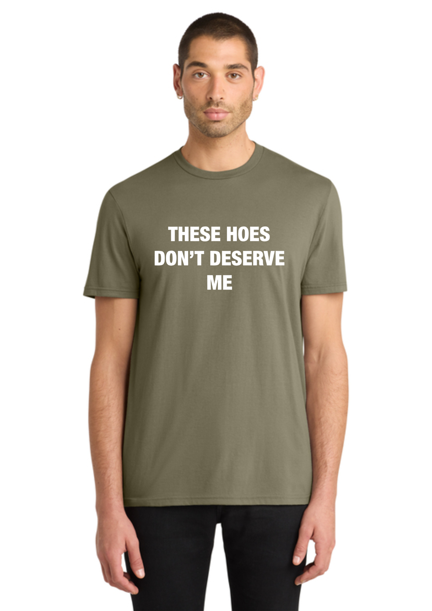 A man wearing an olive green crewneck t-shirt with the text 'THESE HOES DON'T DESERVE ME' printed in white capital letters on the chest, paired with black pants, against a plain white background.